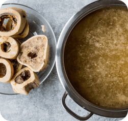 Pot of bone broth with cooked marrow bones on a plate.