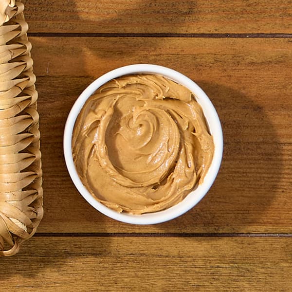 A small container of peanut butter sits atop a picnic table.