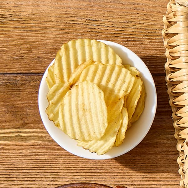 A small collection of salty potatos chips sits on a picnic table amongst other creative S'mores add-ons.