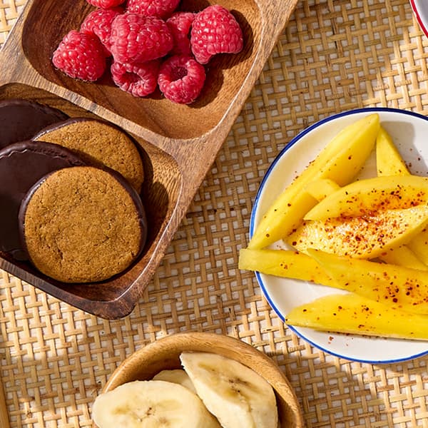 Raspberries, bananas, and sliced mangos with tajin are placed alongside ginger cookies from the Campfire S'mores Kit.