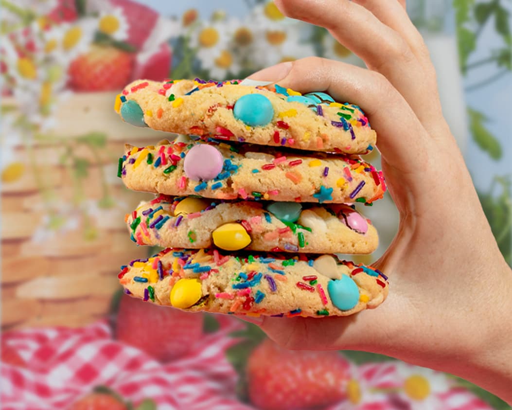 A hand holding a stack of delicious looking baking confetti cookies at a picnic. 
