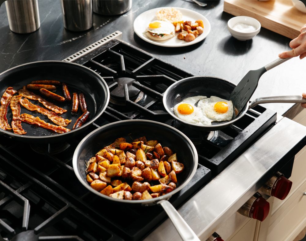 Bacon, sausage, potatoes and eggs cooking in CeramiClad pans on a stovetop