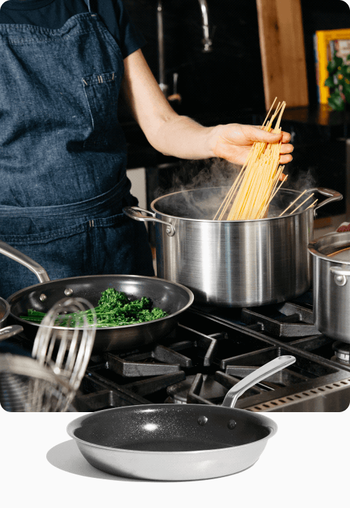 Cook adding herbs to chicken cooking in a CeramiClad saute pan on a gas stove, with a stack of CeramiClad pans and lids below