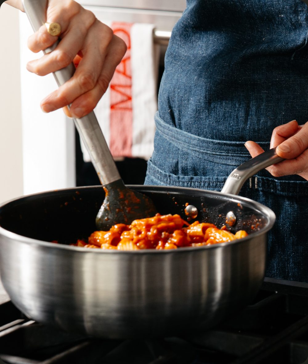 Chef stirring pasta in a stainless clad saucier