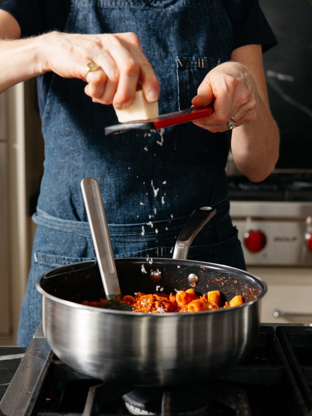 Chef grating cheese over a saucier of pasta