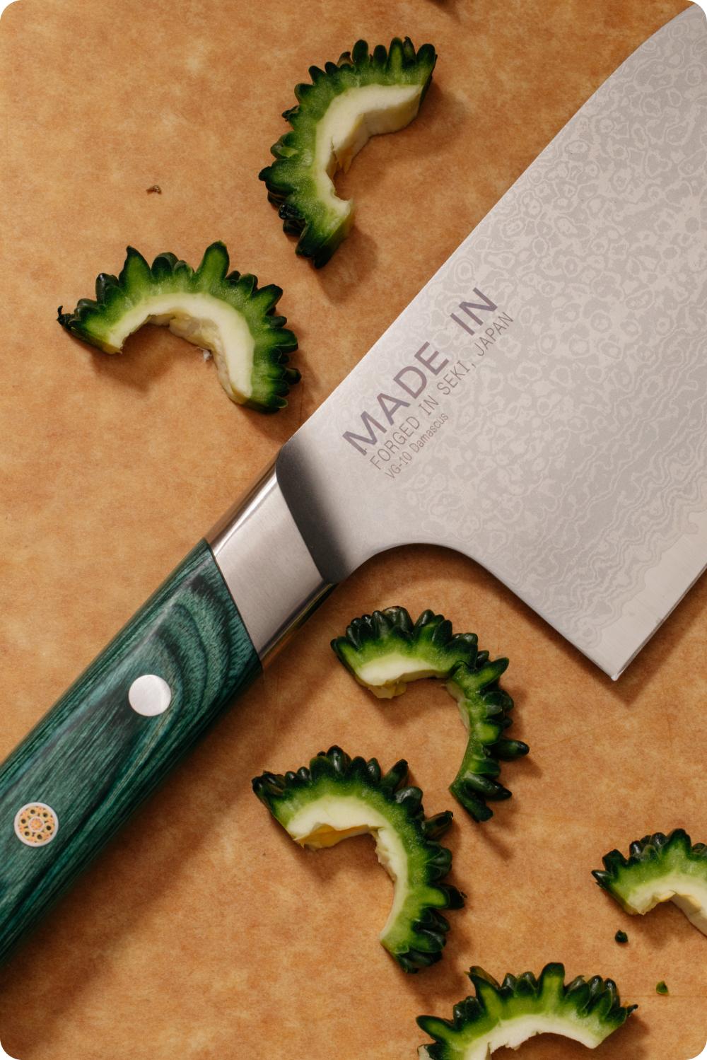 Close-up of the Kamagata Damascus blade beside sliced bitter melon