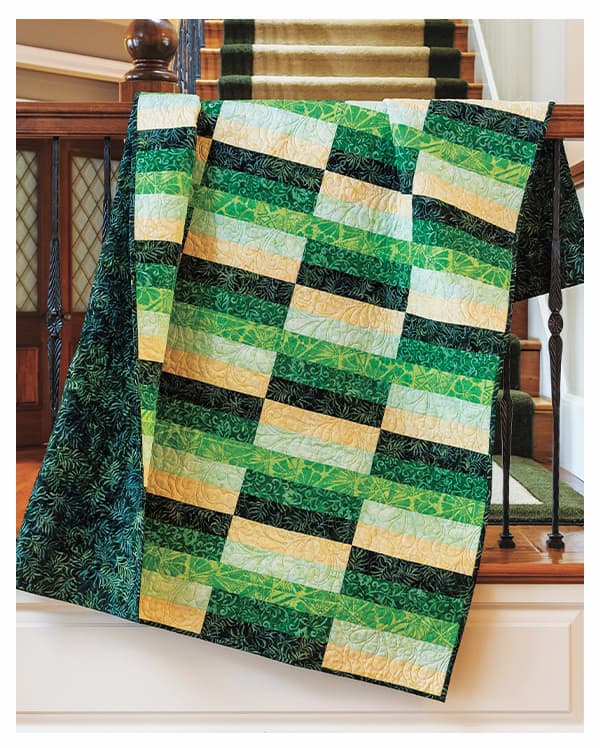 A green and yellow rectangular designed handmade quilt draped over a banister