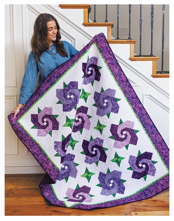 A model holding a purple and white floral shaped handmade quilt