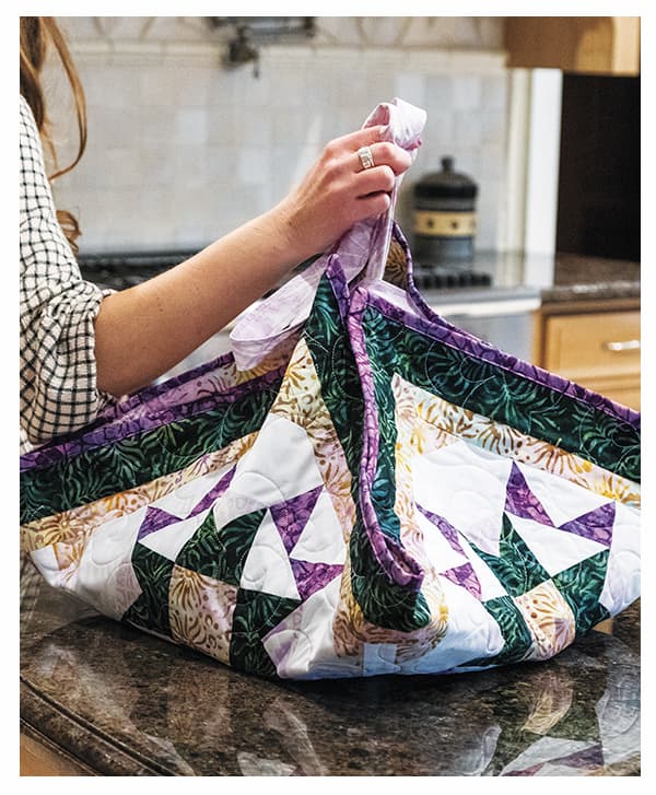 A model holding a green, purple, white, and yellow handmade mini quilt