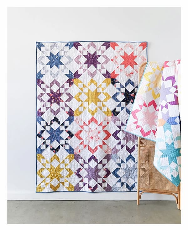 A quilt hanging from a wall, featuring colorful sawtooth blocks on a white background. >>