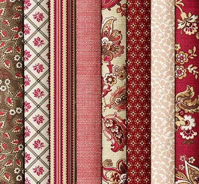 Folded fabrics in reds, creams, and olive greens with florals and striped patterns. >>