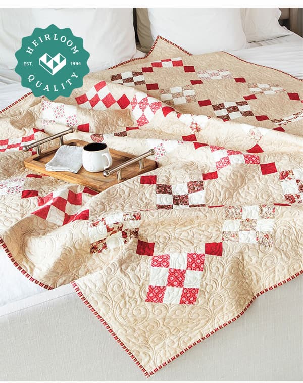 A cream quilt with red squares laying on a bed