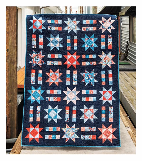 A dark quilt with navy midnight blue background and star and stripe blocks of blues, reds, and whites. >>