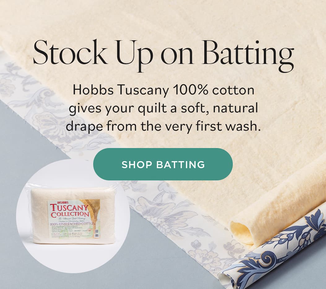 Image: A cut of blue and white floral fabric paired with a cut of cotton batting. Text: Stock Up on Batting. Hobbs Tuscany 100% cotton gives your quilt a soft, natural drape from the very first wash. Shop Batting >>