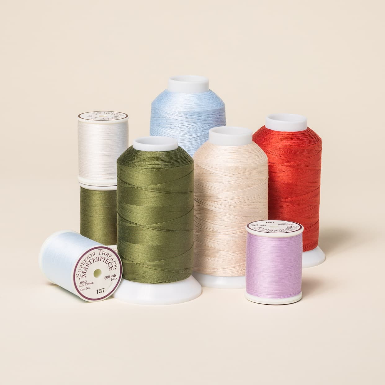 Cones and spools of sewing and quilting thread in greens, pinks, light blues, and creams. >>