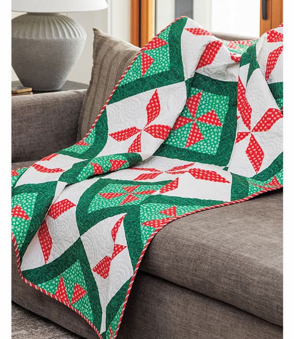 A red, green, and white Christmas themed quilt draped over a couch