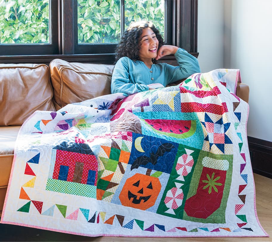 Woman with curly hair sitting on a tan couch with a holiday quilt over here