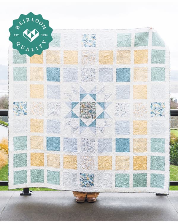 A person holding a blue white and green handmade quilt