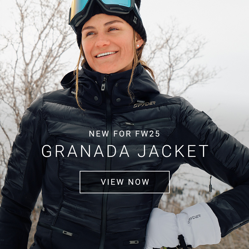 Female skier wearing a black ski jacket with insulation baffles against a forest backdrop.