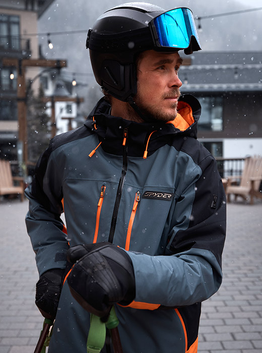Skier, River Radamus, wearing the Vyper Jacket in Slate Blue in a resort town background