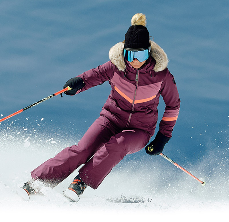 Ski action photo of the Primrose Jacket with hood down and fur trim visible on blue background