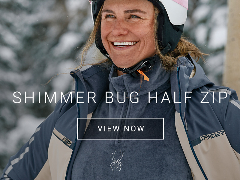 Female skier smiling with a open jacket presenting a soft half zip sweater with a shimmer bug Spyder logo.
