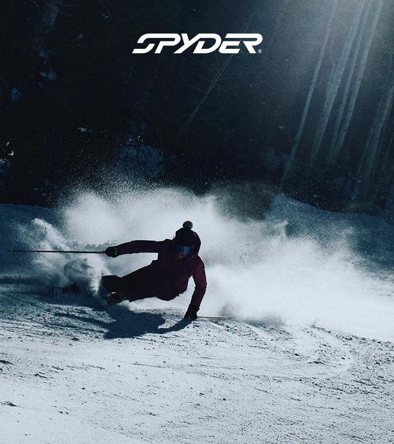 Skier in a dark moody environment, light shining down. Spyder For Skiers Since 1978