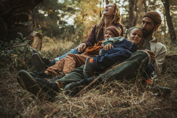  A woman and a man lie in dry grass on a forest floor with two children between them. All four are smiling. They wear casual autumn clothing and Wildling shoes.