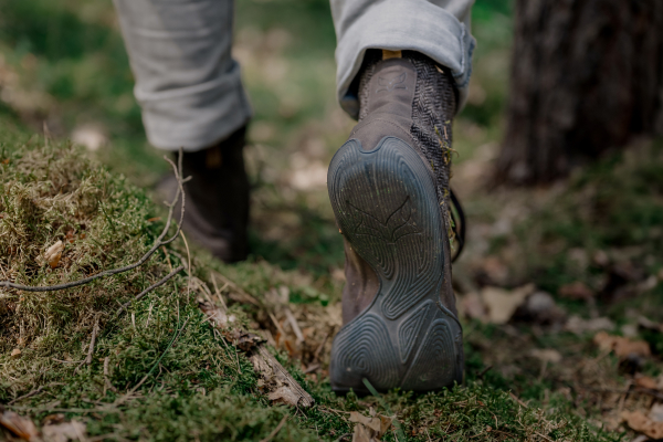 A person walks across a mossy forest floor. Only their lower legs and feet are visible. They are wearing rolled-up grey jeans and Wildling Kindur Sten.