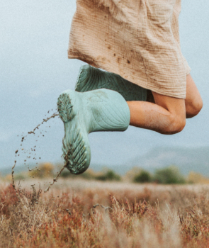 The picture shows a close-up of a woman jumping. She is wearing Ranidae rain boots, and some mud is splashing up