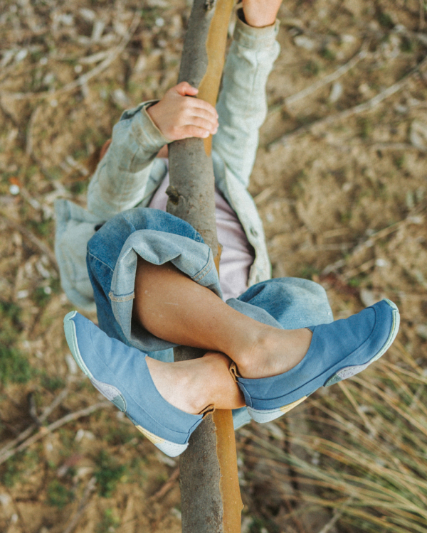 The picture shows a person hanging upside down from a branch, holding on with her feet and legs. She is wearing the Kami Mizu model.