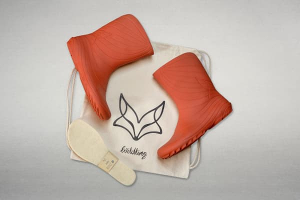 Red Wildling Ranidae rain boots placed on a Wildling fabric tote bag, with the Felty wool insole beside them.
