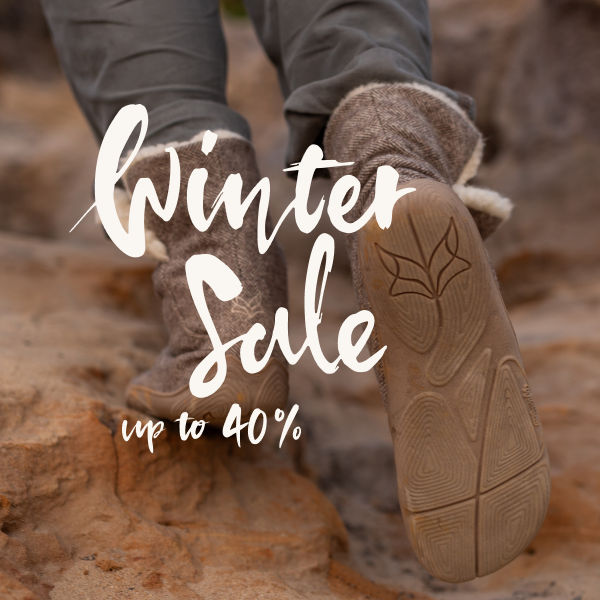 A person walks over a stone wearing Koselig. Only their lower legs, the backs of their soles and the words ‘Winter Sale up to 40%’ are visible.