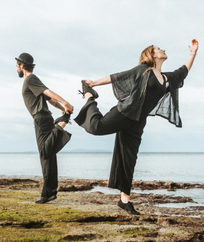 The picture shows a man and a woman dancing by the sea; they are dressed in black and are wearing Tanuki Yoru