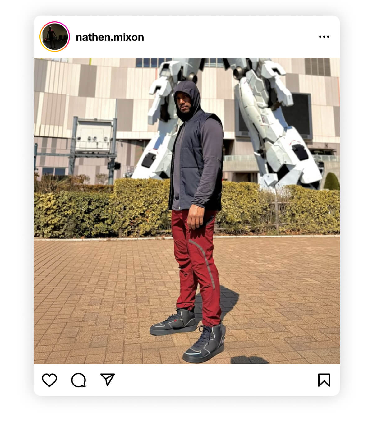 Man in a hoodie and red pants stands confidently in front of a giant robot statue, creating a bold and dynamic atmosphere with sunny weather.