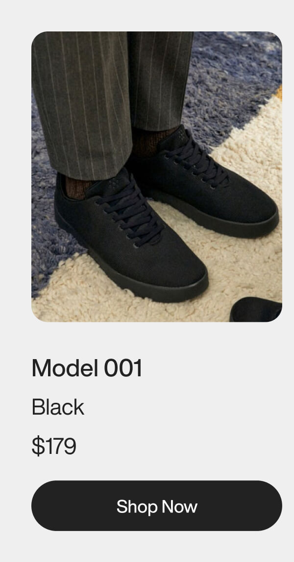 Man wearing black sneakers with pinstripe pants on a textured rug. Text reads "Model 001 Black" with a "Shop Now" button below.