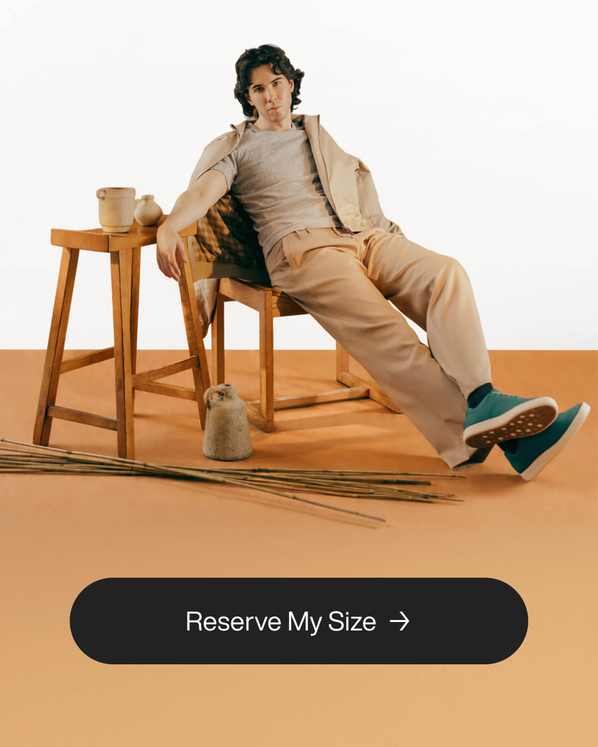 A relaxed man in beige clothes leans on a wooden chair. Pottery and reeds are nearby on an earthy-toned backdrop. Text reads, "Secure My Size."