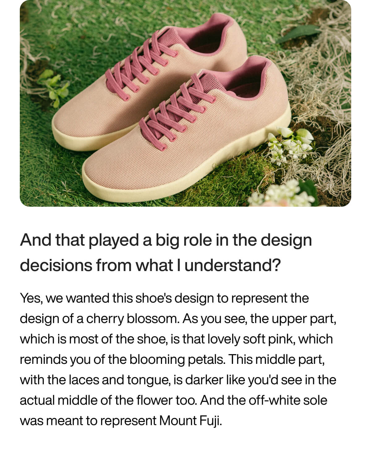 A pair of pink sneakers with darker pink laces rests on grass, accompanied by small white flowers. The design is inspired by cherry blossoms.