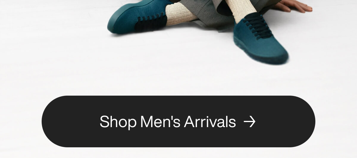 Casually dressed person seated, wearing teal sneakers with beige socks and gray pants. A button below reads "Shop Men's Arrivals" on a black background.