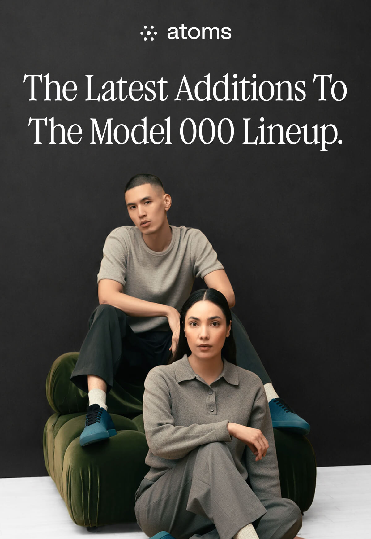 Two models in grey outfits pose on a green chair against a dark background. Text above reads, "The Latest Additions To The Model 000 Lineup."