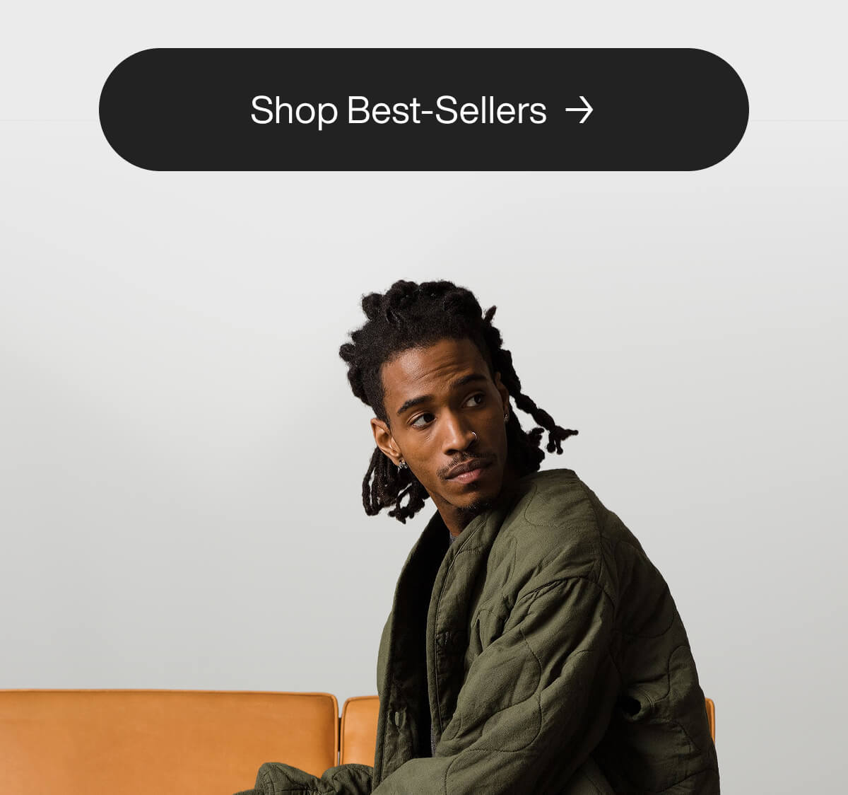 "Man in green jacket sits on a tan couch, looking to the side. Above, a button reads "Shop Best-Sellers" with an arrow."