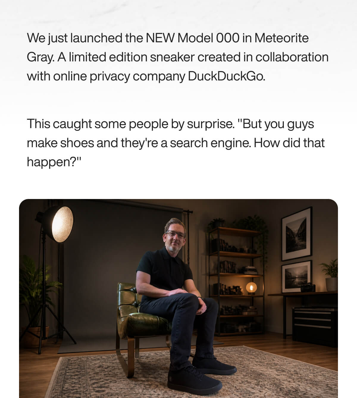 A person sits on a green chair in a warmly-lit room, wearing black sneakers. A text above mentions a shoe collaboration with DuckDuckGo.