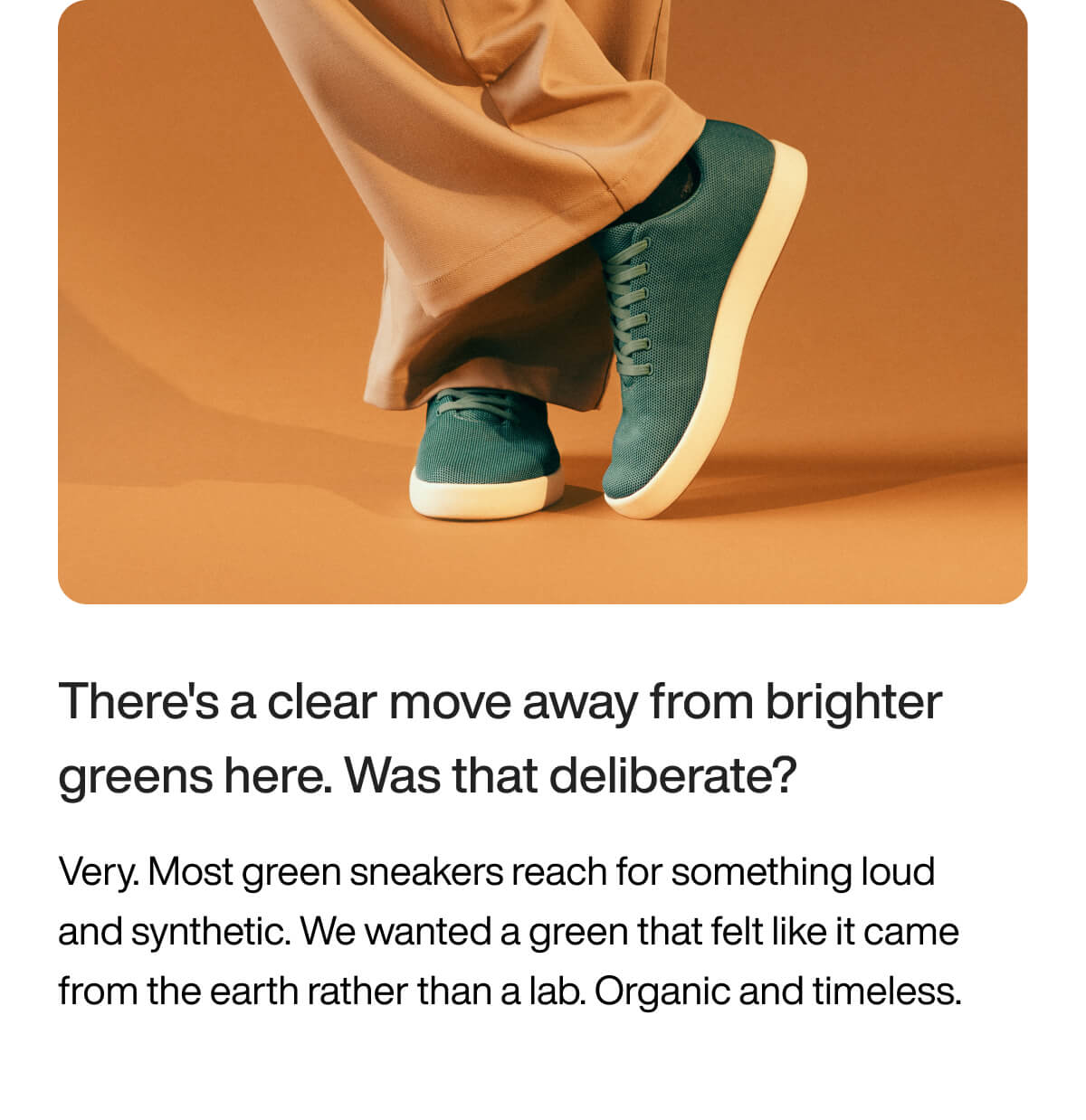 Person wearing beige pants and green sneakers with white soles stands on an orange background. The tone is natural and earthy, highlighting simplicity.