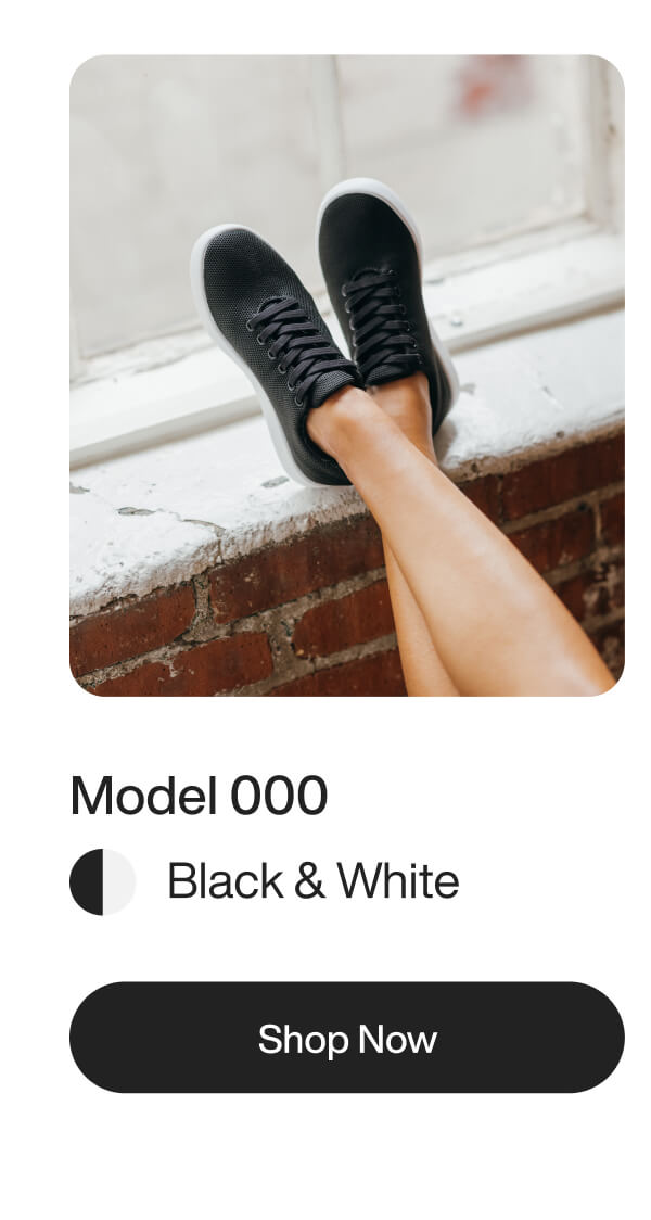 Female legs in black and white sneakers rest on a windowsill. Brick wall backdrop. Text reads "Model 000, Black & White, Shop Now." Casual and stylish feel.