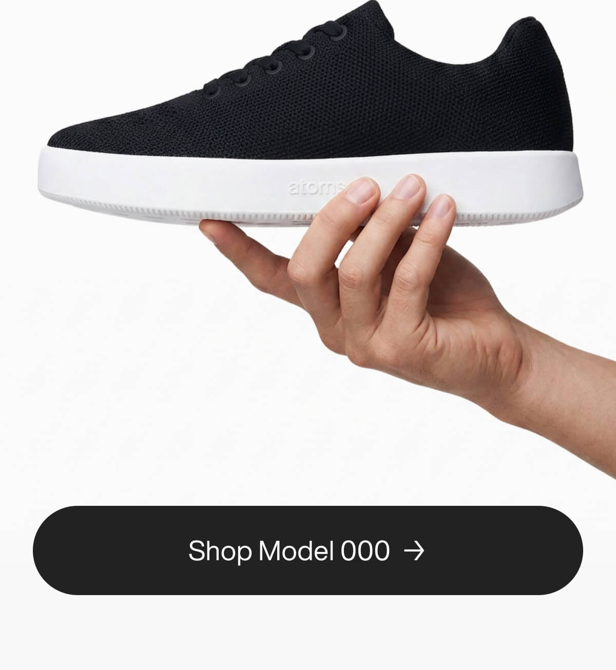 A hand holds a sleek black sneaker with a white sole against a plain background. The shoe's lightweight design is emphasized by the relaxed hand grip. Text below reads "Shop Model 000."