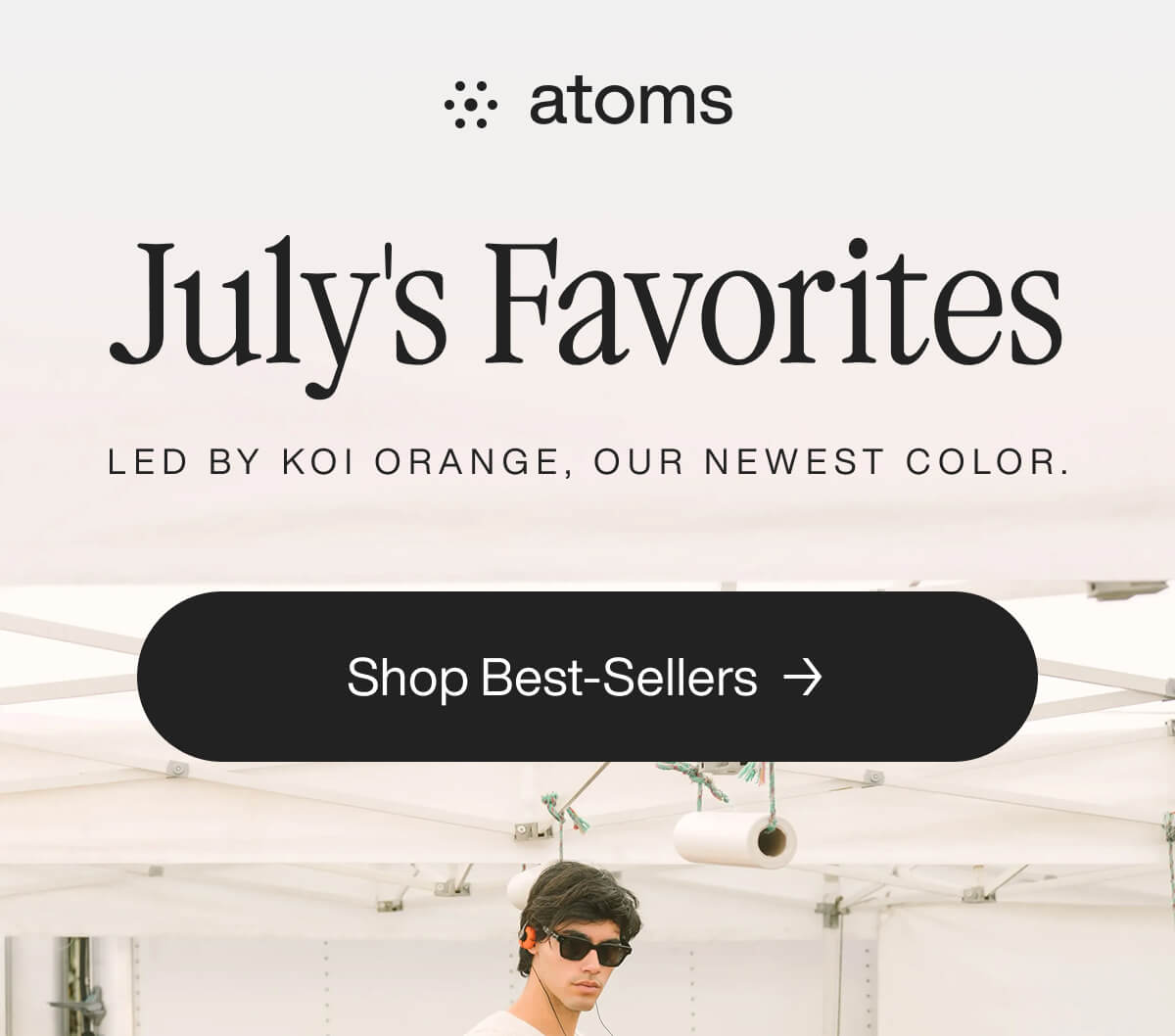 Text reads "July's Favorites" with a focus on "Koi Orange, our newest color." A button below says "Shop Best-Sellers." A person wearing sunglasses is underneath.