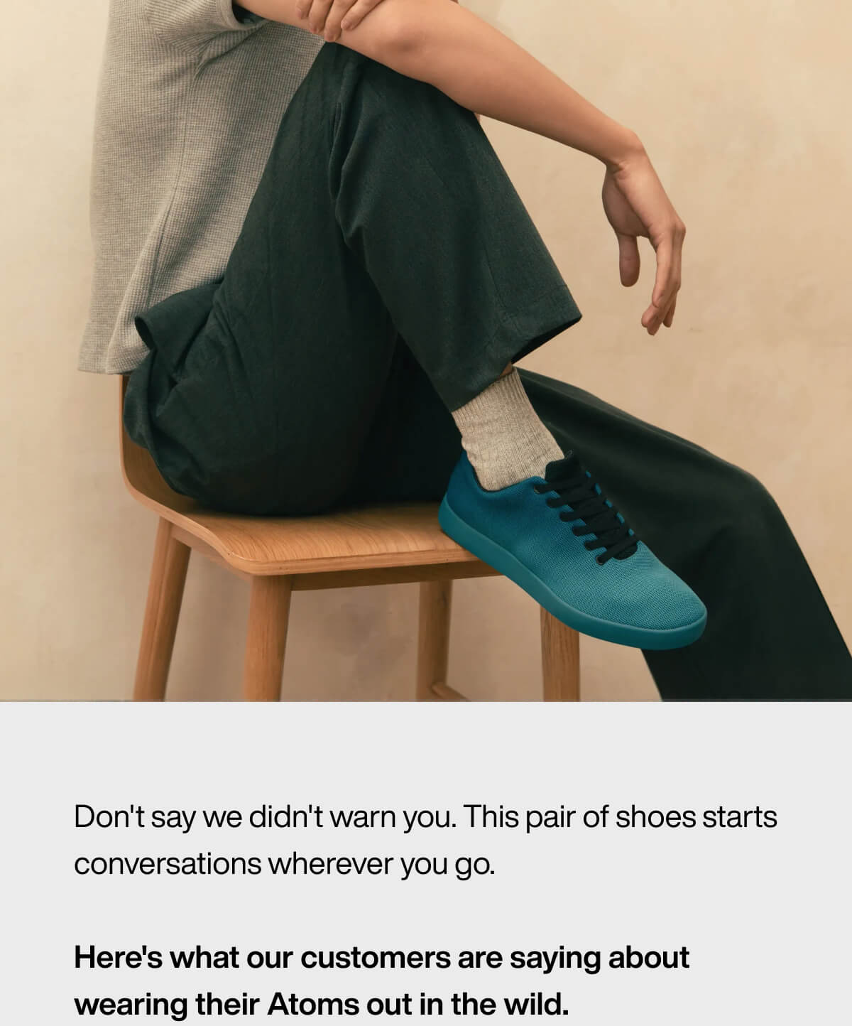 "Person seated on a chair, wearing teal Atoms shoes, gray socks, dark pants, and a light top, with arms resting on knees."