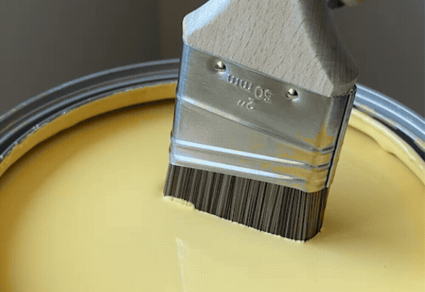 Paint brush dipping into Golden Hour yellow paint