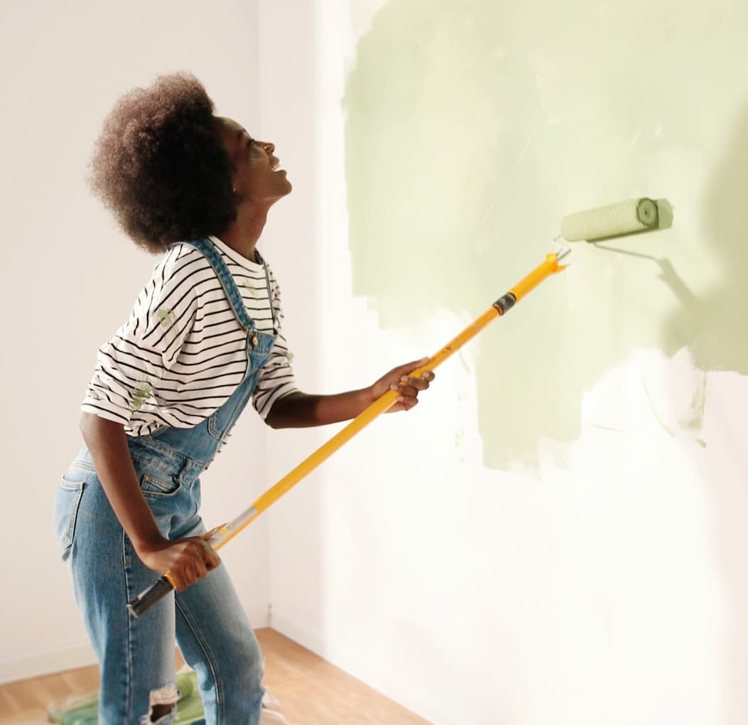 Woman using roller with extension pole to paint the wall