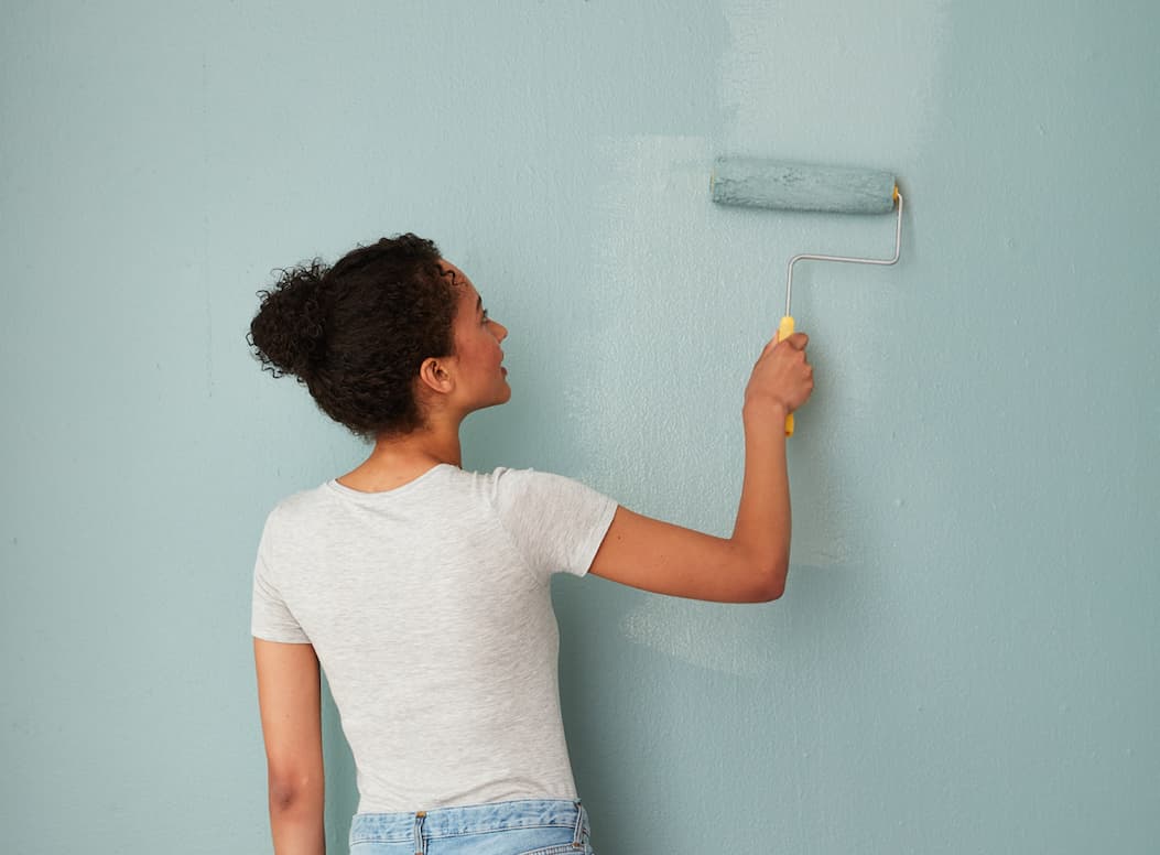 Woman rolling green blue paint onto wall with paint roller